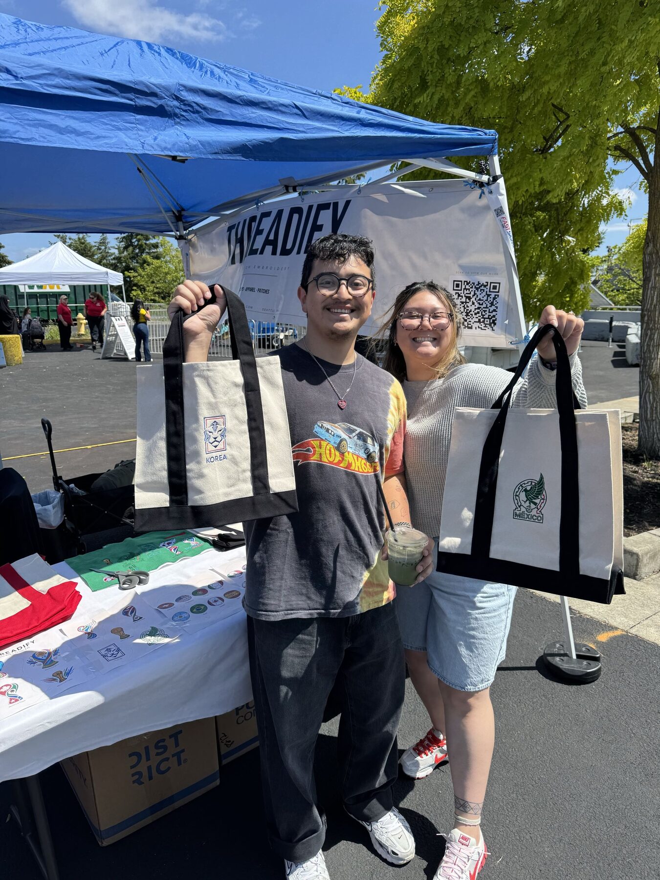 Justin Kaiponen and Alex Chan at the Threadify booth holding custom embroidered totes